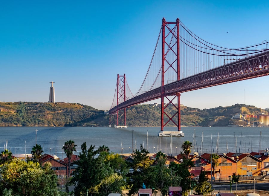 View of the 25 de Abril Bridge in Lisbon with the Cristo Rei statue in the background and the Tagus River in the foreground — one of the city’s most iconic landmarks connecting Lisbon and Almada.