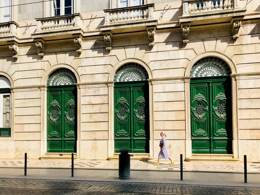 Classic Lisbon facade with ornate green doors and traditional architectural details, bathed in warm sunlight.
