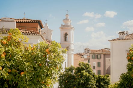 Typical Lisbon view with orange trees and traditional Portuguese architecture, featuring a historic church tower and tiled rooftops under a bright blue sky.
