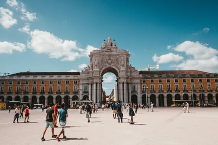 Rua Augusta Arch at Praça do Comércio in Lisbon, with tourists walking on a sunny day.