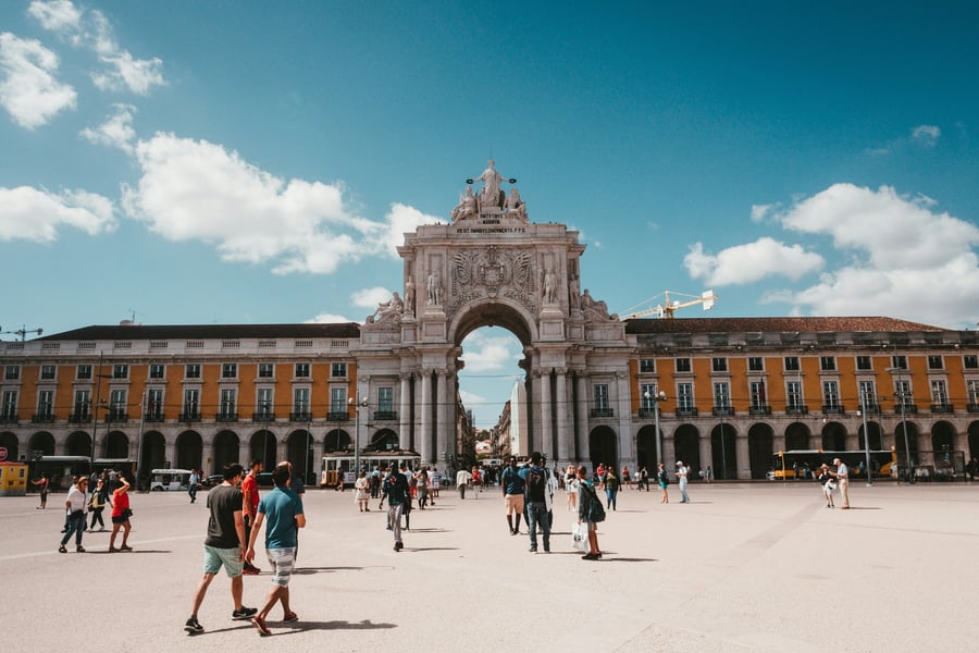 Rua Augusta Arch at Praça do Comércio in Lisbon, with tourists walking on a sunny day.