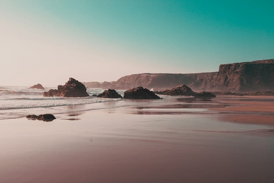 Wild beach on the Vicentine Coast in Portugal, with rocks in the sea and cliffs in the background at sunset.