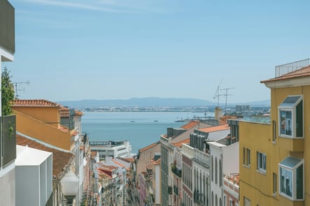 Panoramic view of Lisbon with traditional orange rooftops and the Tagus River in the background, showcasing lifestyle and real estate investment opportunities in Portugal.