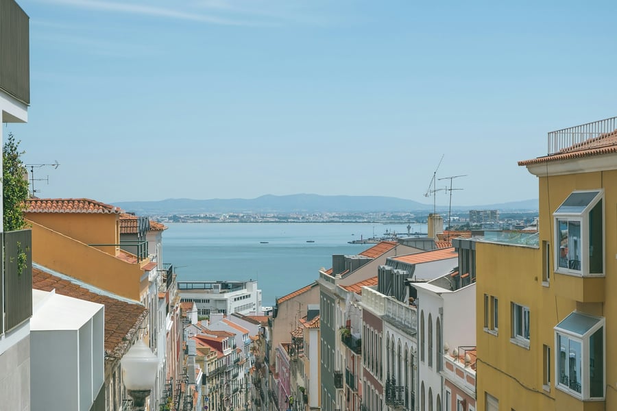 Panoramic view of Lisbon with traditional orange rooftops and the Tagus River in the background, showcasing lifestyle and real estate investment opportunities in Portugal.