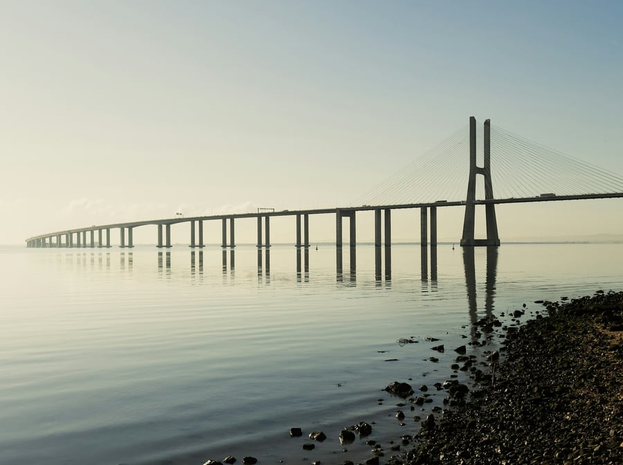 Panoramic view of Vasco da Gama Bridge in Lisbon, Portugal, reflected on the calm waters of the Tagus River on a bright morning.