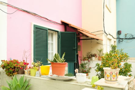 Colorful facade of a Portuguese house with pink and blue walls, green shutters, and potted plants on the patio, typical of small towns in Portugal.