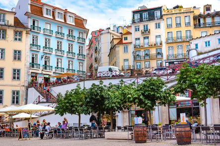 Lively café terrace at Largo do Carmo in Lisbon, surrounded by colorful buildings and traditional Portuguese architecture on a sunny day.