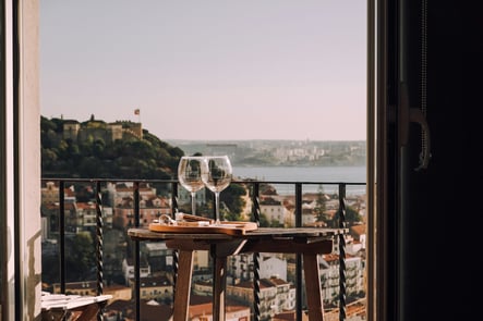 Balcony overlooking Lisbon with two wine glasses and São Jorge Castle in the background, capturing the charm and lifestyle of Portugal.