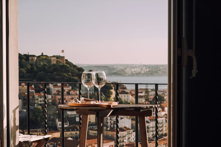 Balcony overlooking Lisbon with two wine glasses and São Jorge Castle in the background, capturing the charm and lifestyle of Portugal.