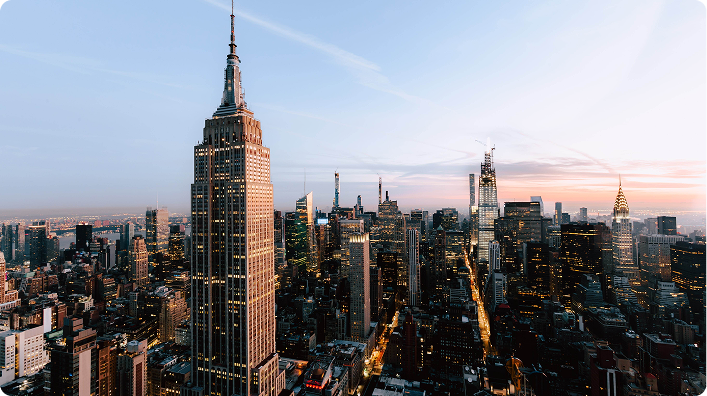 Panoramic view of New York City at sunset with the Empire State Building and illuminated skyscrapers.